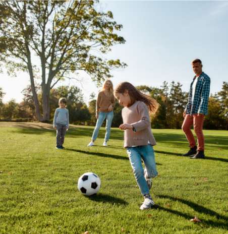 Dzieci grajązy w piłkę z rodzicami na zielonej trawie.